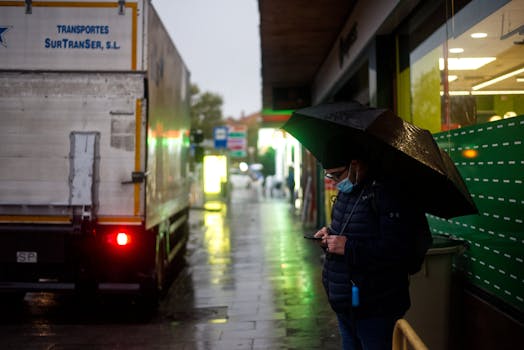 A man stands under an umbrella on a rainy street using his phone in Pozuelo de Alarcón, Spain.
