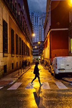 A person crosses a dimly lit street in Madrid, showcasing urban life in the evening.