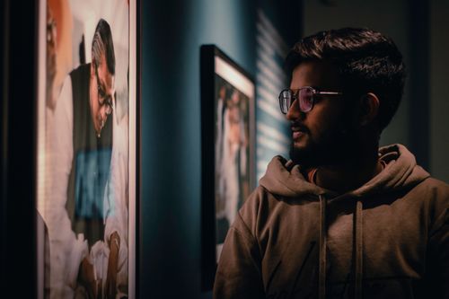 Free Man examining framed artwork in a gallery in Dhaka, Bangladesh. Mood lighting enhances the cultural setting. Stock Photo