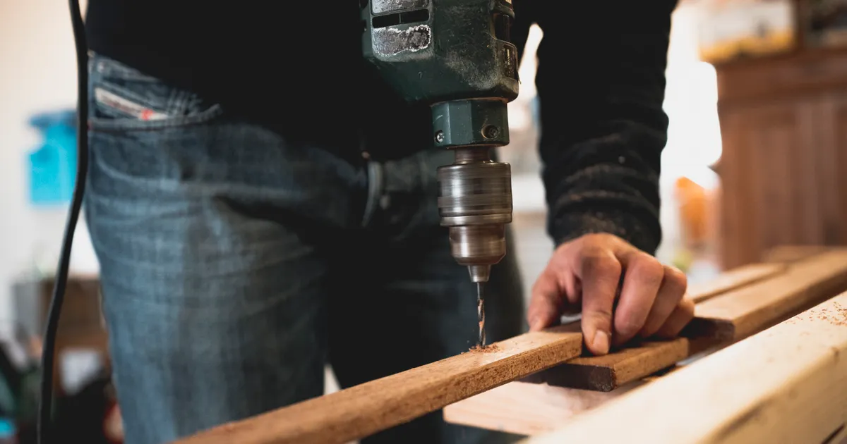 Man using a power drill on a wooden board in a workshop
