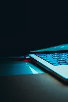 Close-up of a glowing laptop keyboard and lid in a dark setting, highlighting technology and design.