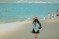 一位戴着帽子和太阳镜的女子走在阳光明媚的海边沙滩上