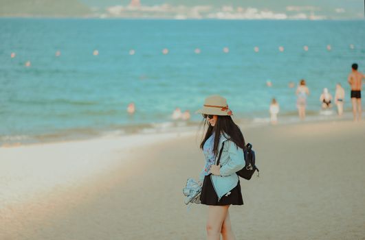 一位戴着帽子和太阳镜的女子走在阳光明媚的海边沙滩上