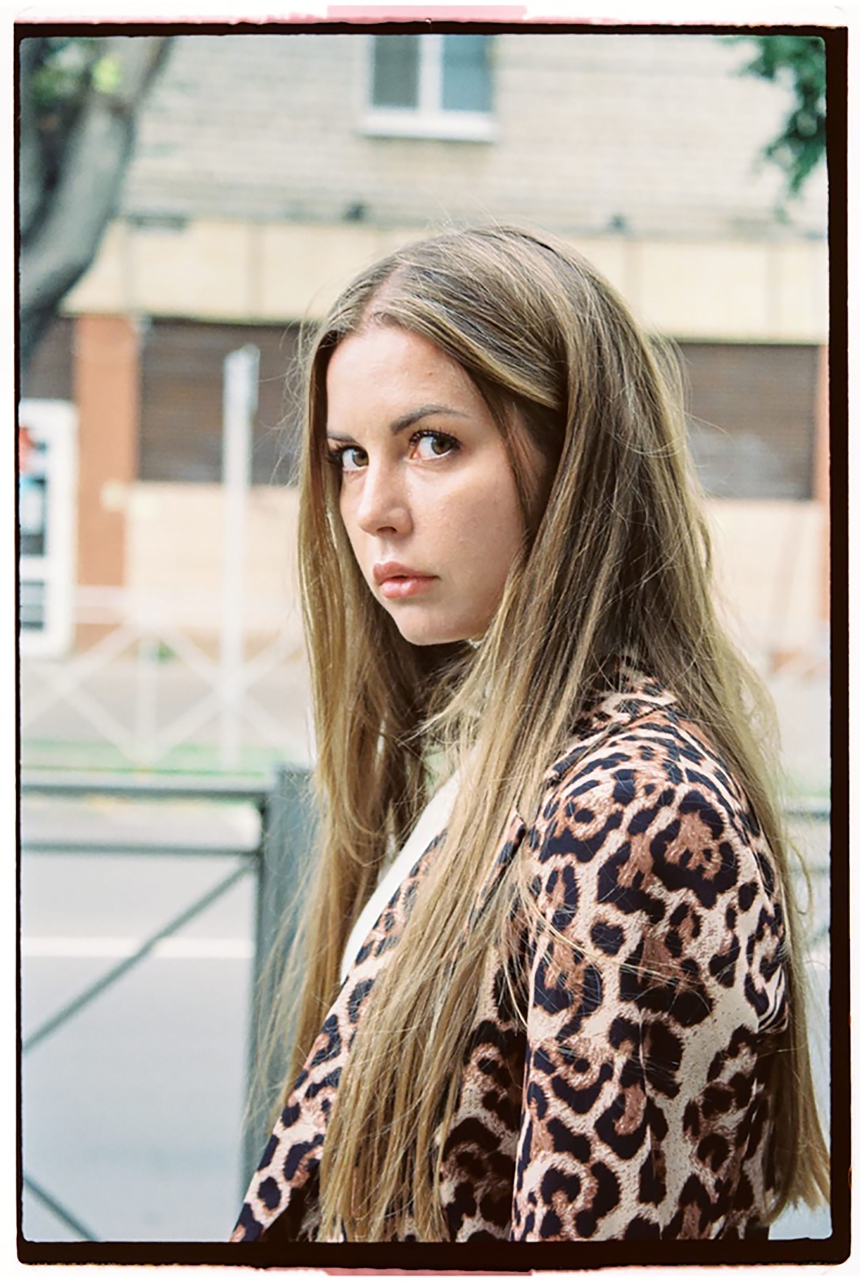 A young woman in a leopard print jacket poses outdoors with a blurred background.