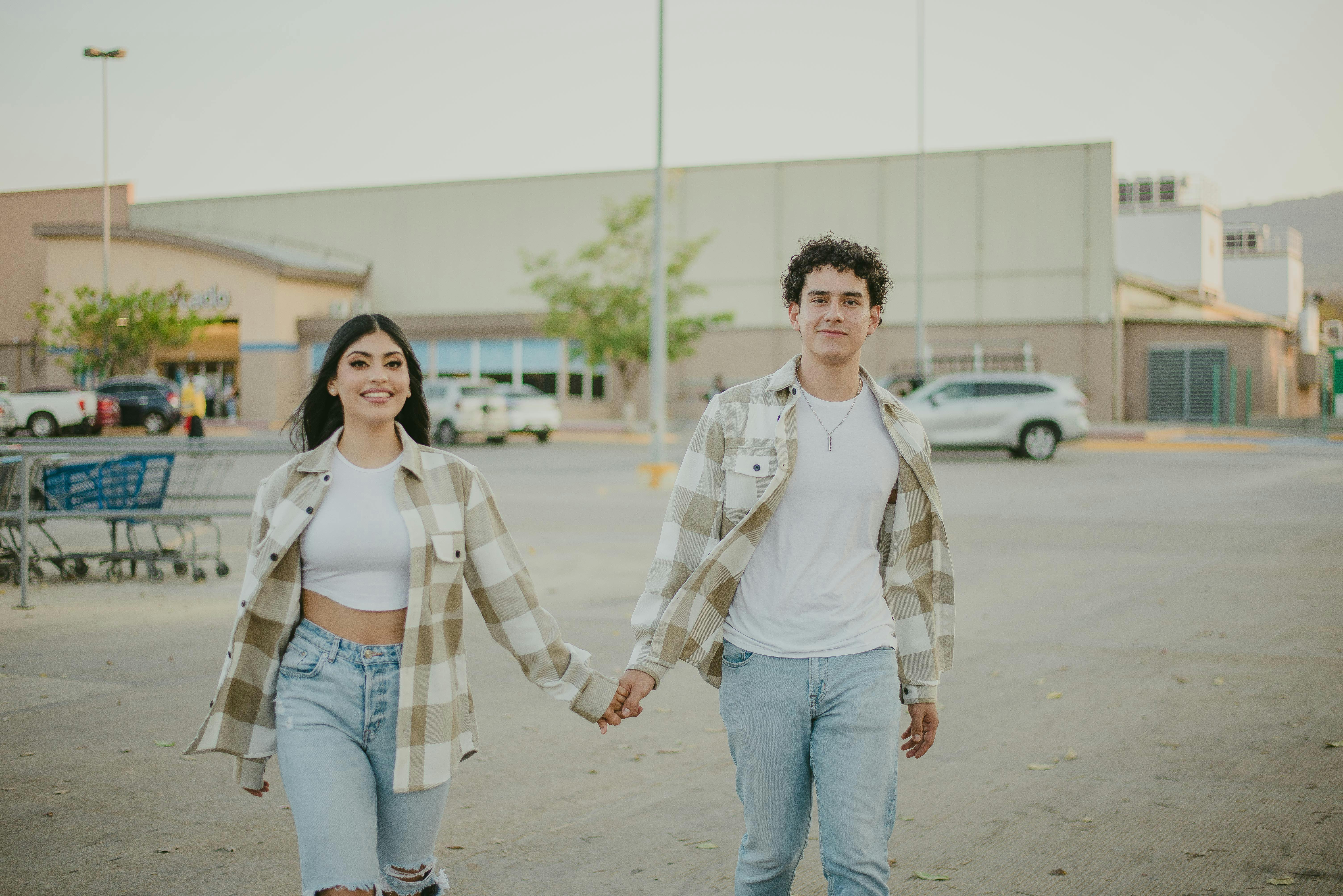 A couple with matching outfits holding hands and smiling in a parking lot.