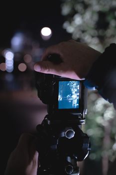 A hand holding a camera capturing a night scene with bokeh effect and blurred background.
