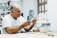 一位资深男工匠在光线充足的工作室里，正专心地用各种创意工具制作雕塑