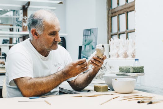 一位资深男工匠在光线充足的工作室里，正专心地用各种创意工具制作雕塑