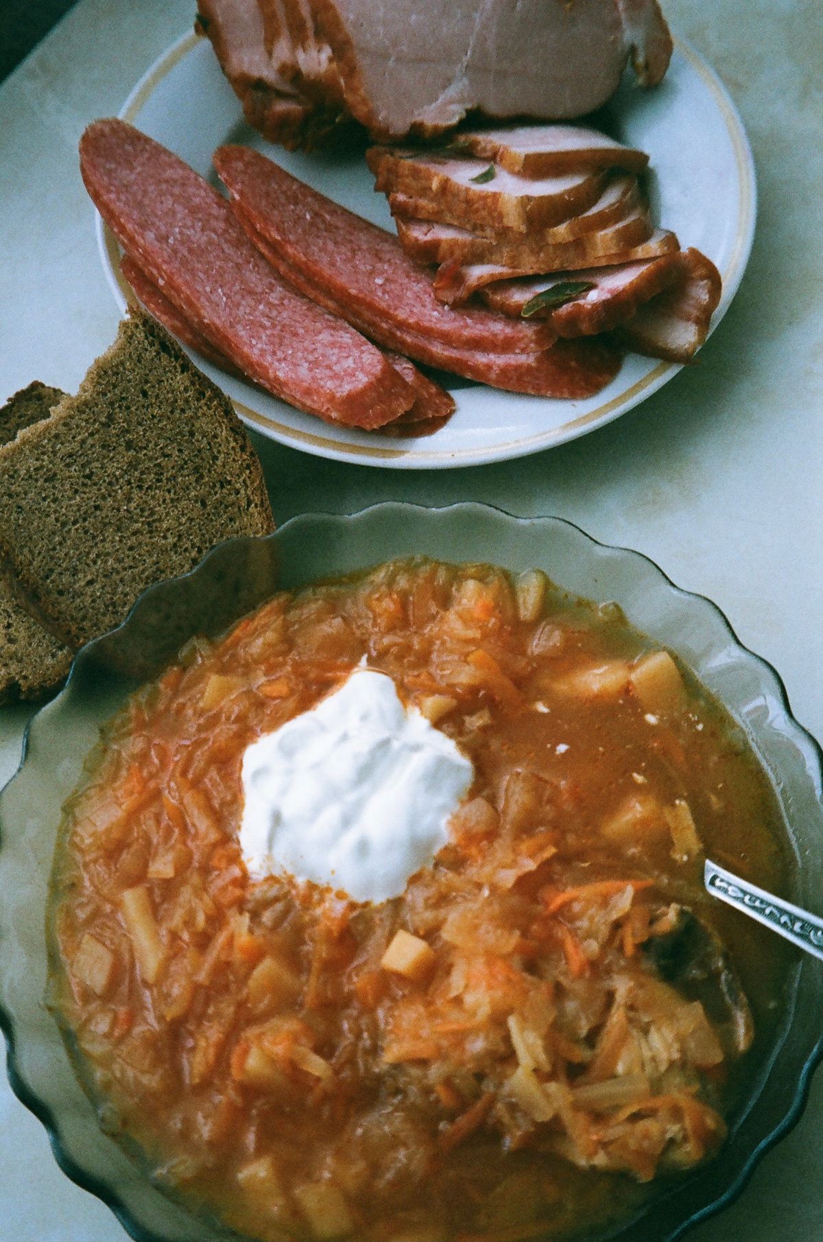 Winter soup recipes: a bowl of cabbage soup with sour cream next to rye bread and sliced meats
