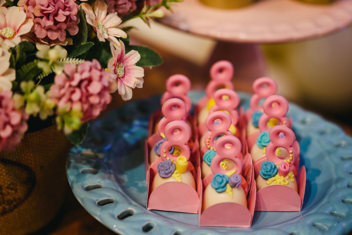Pink decorated candies with floral accents elegantly displayed on a blue ceramic plate beside a bouquet.