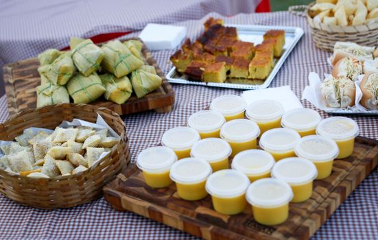 An assortment of traditional dishes including corn cake, tamales, and dessert cups on a checkered table.