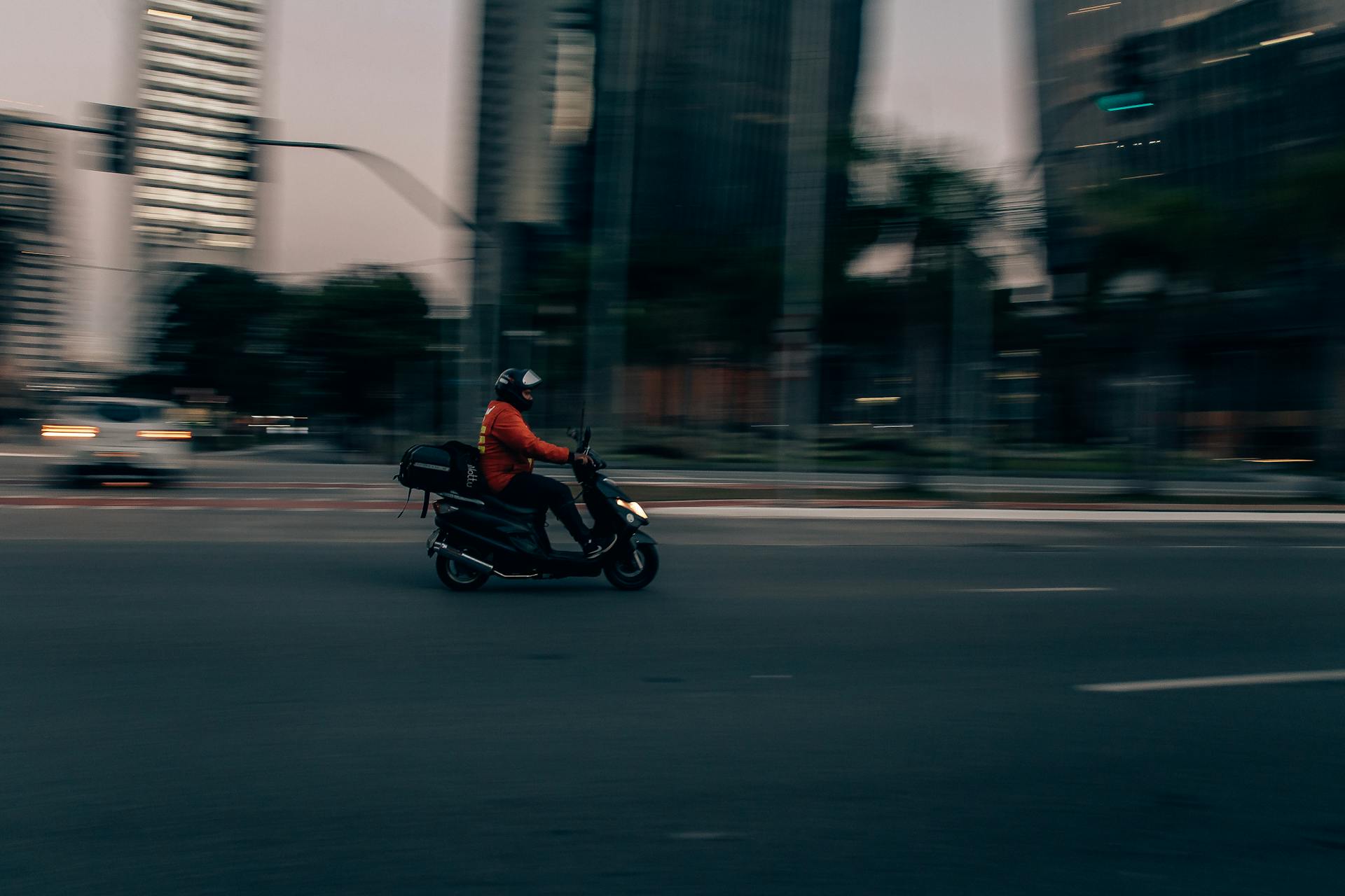 Blurred motion of a delivery scooter on São Paulo street at dusk, capturing urban hustle.