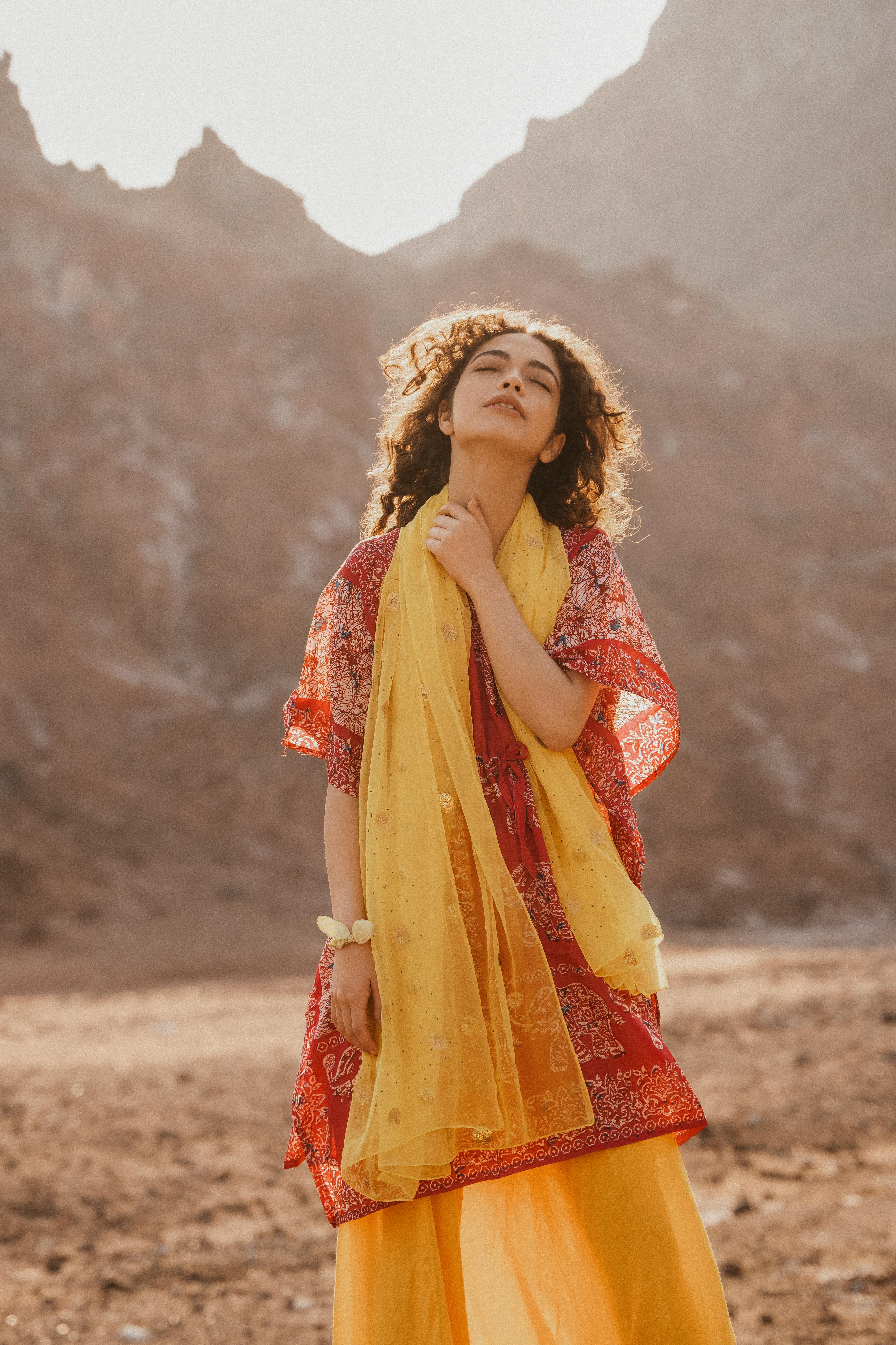 Woman in colorful dress and scarf standing peacefully in desert landscape.