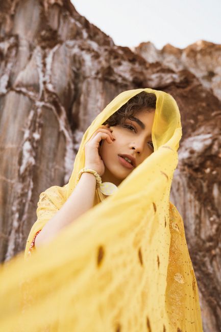 Portrait of a woman wearing a yellow shawl with a rocky backdrop, exuding elegance and grace.