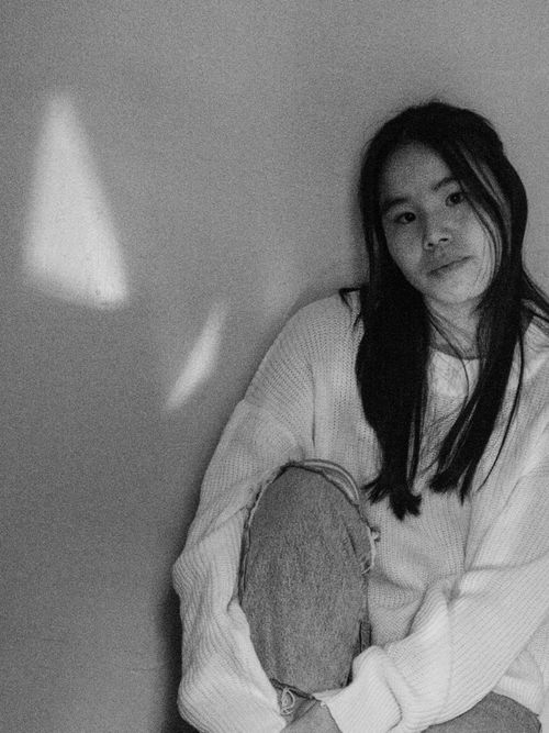 Free Black and white portrait of an Asian woman in a knitted sweater sitting pensively against a wall. Stock Photo