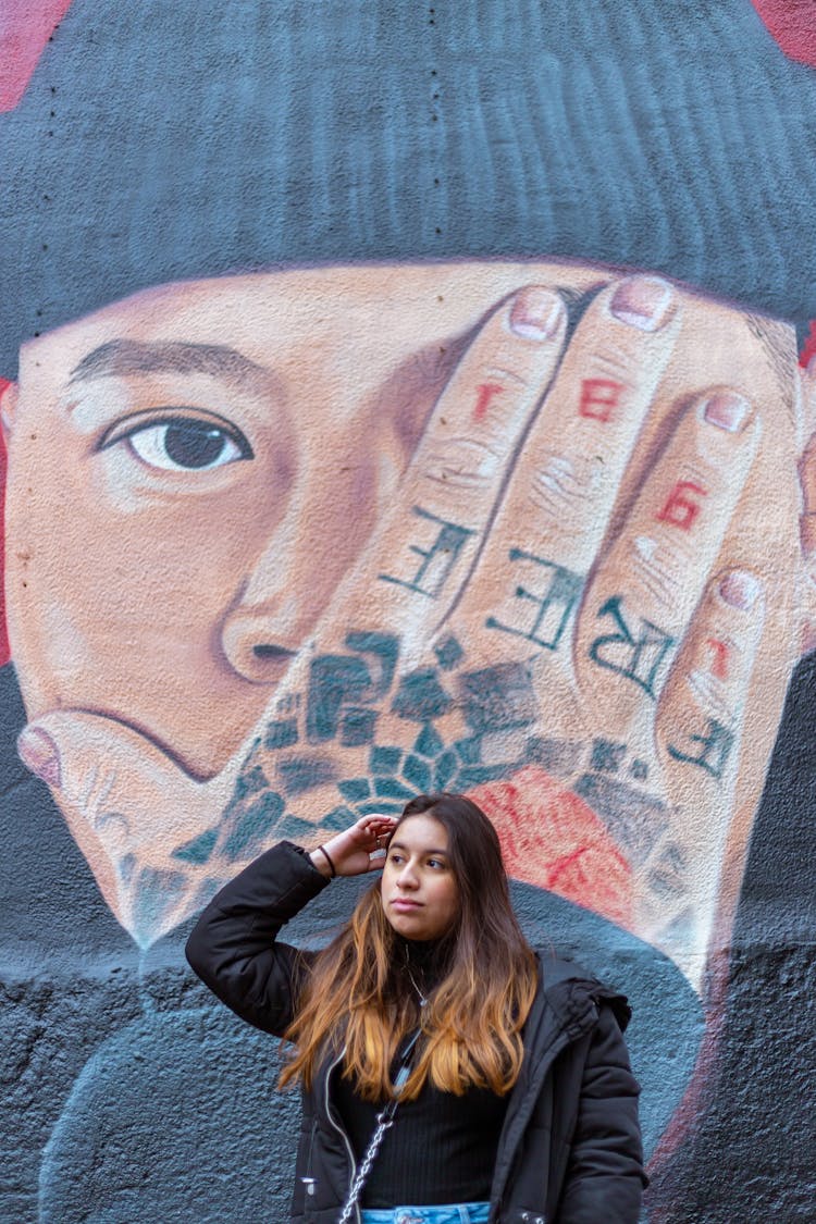 Woman Posing By Mural Of Man With Hand On Face