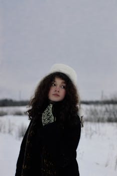 Woman wearing winter clothing, looking away in a snowy landscape. Perfect for seasonal and fashion themes.