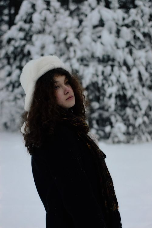 Free Woman in a hat standing in a snowy forest, exuding winter charm. Stock Photo