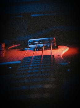 Intimate close-up of a bass guitar bathed in red light, highlighting its strings and structure.