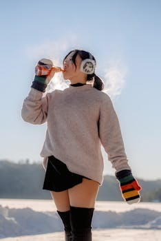 A woman in winter attire drinks from a bottle against a snowy backdrop.