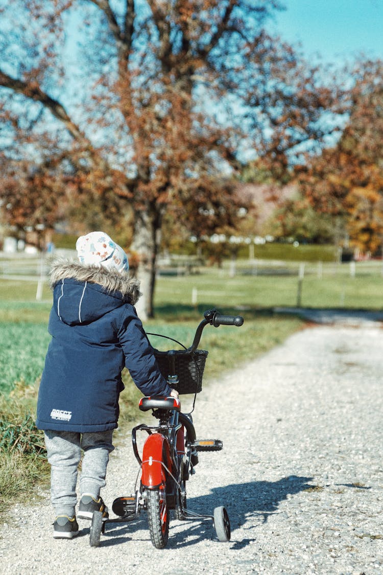 Child Leading Bicycle On Dirt Road