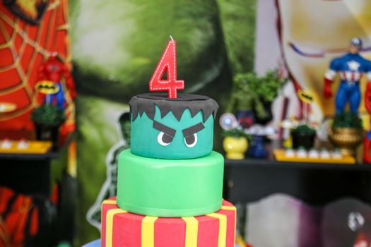 Two-tier superhero themed birthday cake topped with a number four candle, perfect for children's parties.