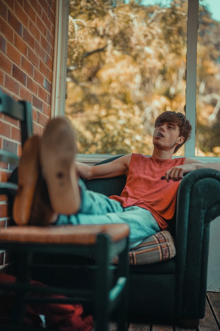 A Young Man Sitting In A Sofa Chair While Vaping