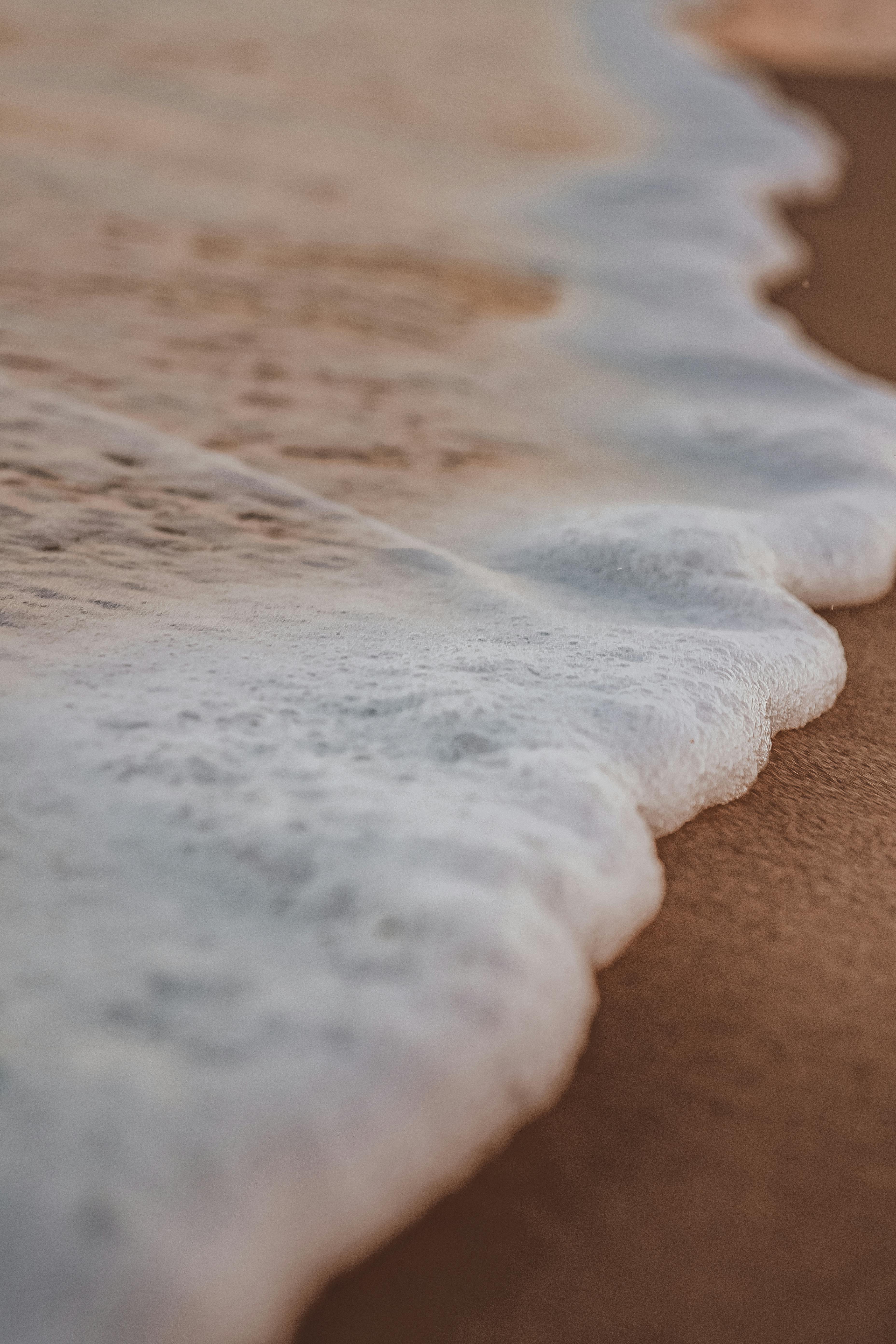 Close-up of tranquil waves gently washing over sandy beach with selective focus.