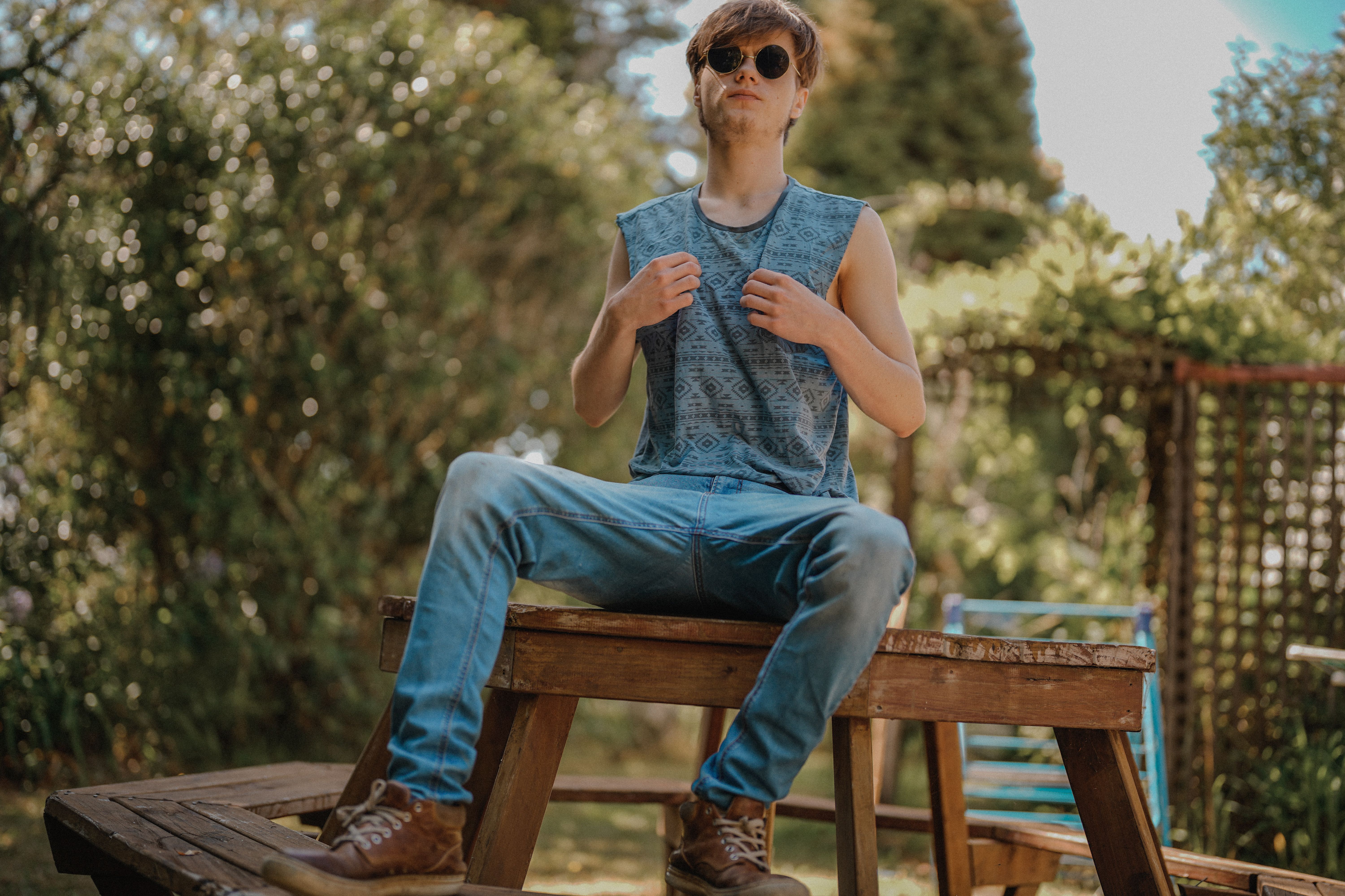 Young man in sleeveless shirt and sunglasses sitting confidently on a bench outdoors.