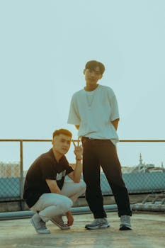 Two fashionable men posing together outdoors during sunset with a stylish urban backdrop.