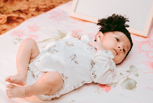 Free Baby in White and Pink Floral Onesie Lying on White and Pink Floral Bed Stock Photo