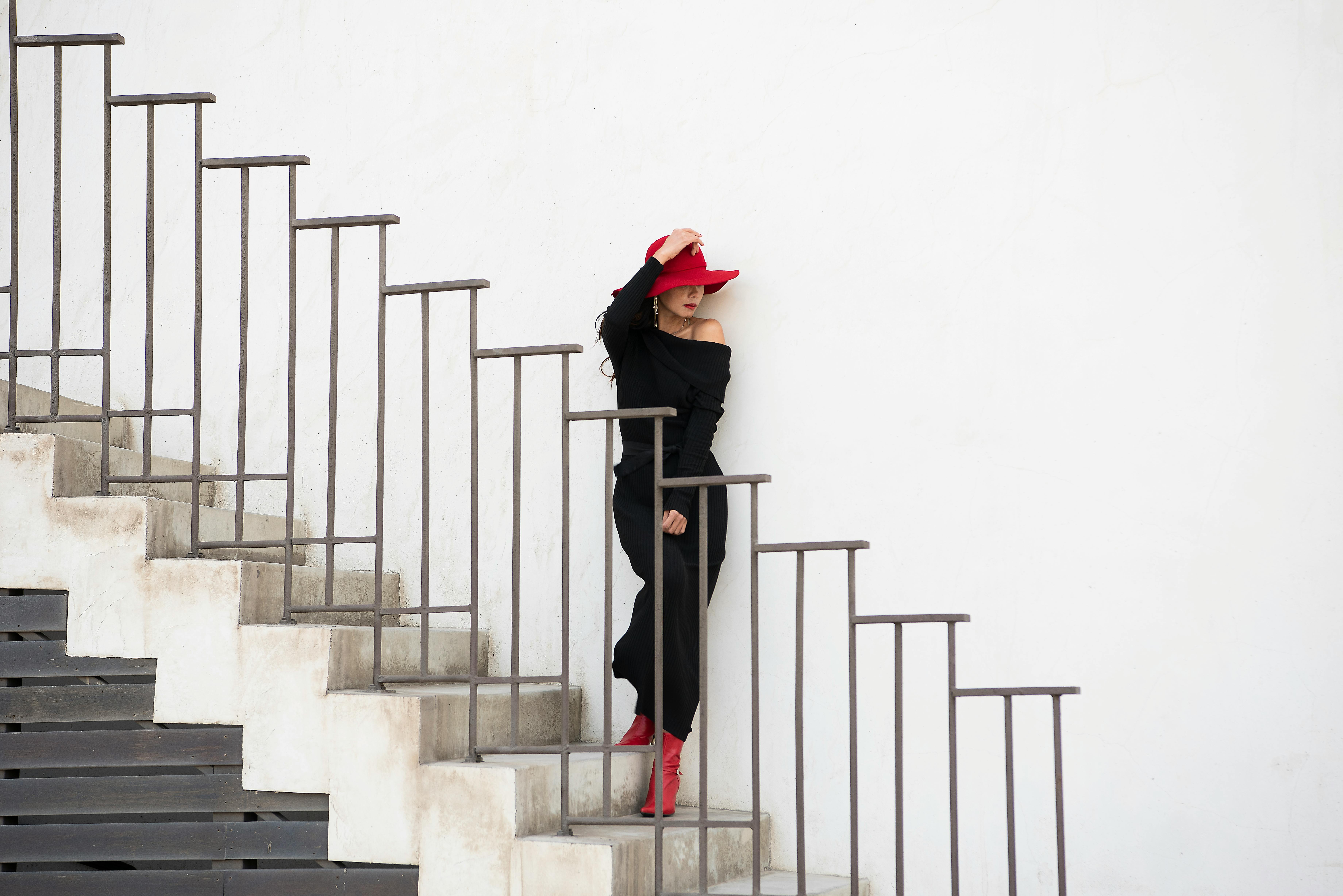 Elegant woman in black with a red hat poses stylishly on a modern staircase