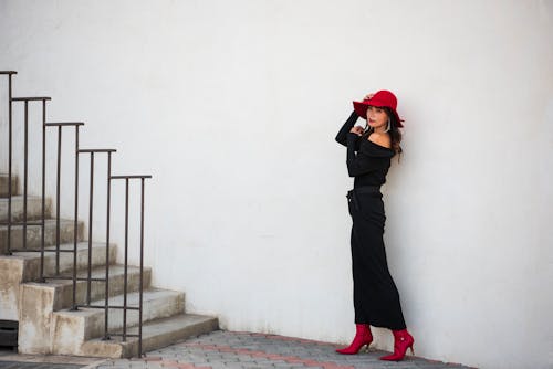 Woman in a Dress and a Hat Posing by a White Wall