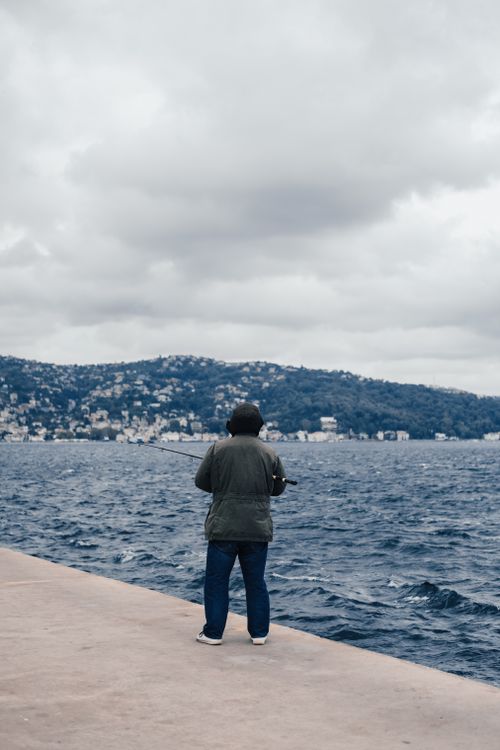 Free A man enjoys fishing on a pier by the Bosphorus in Istanbul, under cloudy skies. Stock Photo