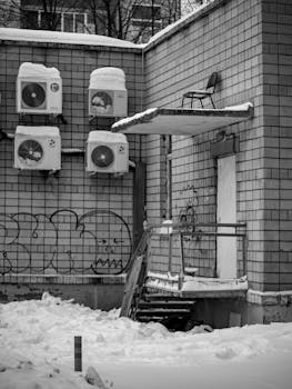 Black and white urban winter scene showcasing graffiti, air conditioners, and a snow-covered ground.