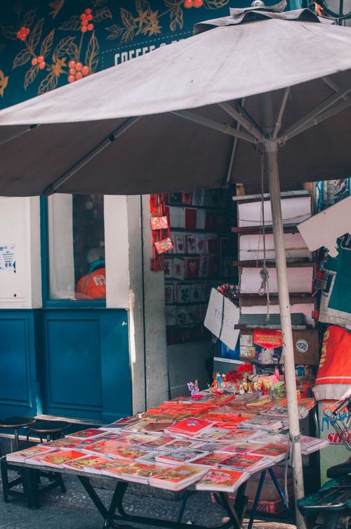 Free Vibrant outdoor street market stall selling various goods under a large umbrella. Stock Photo