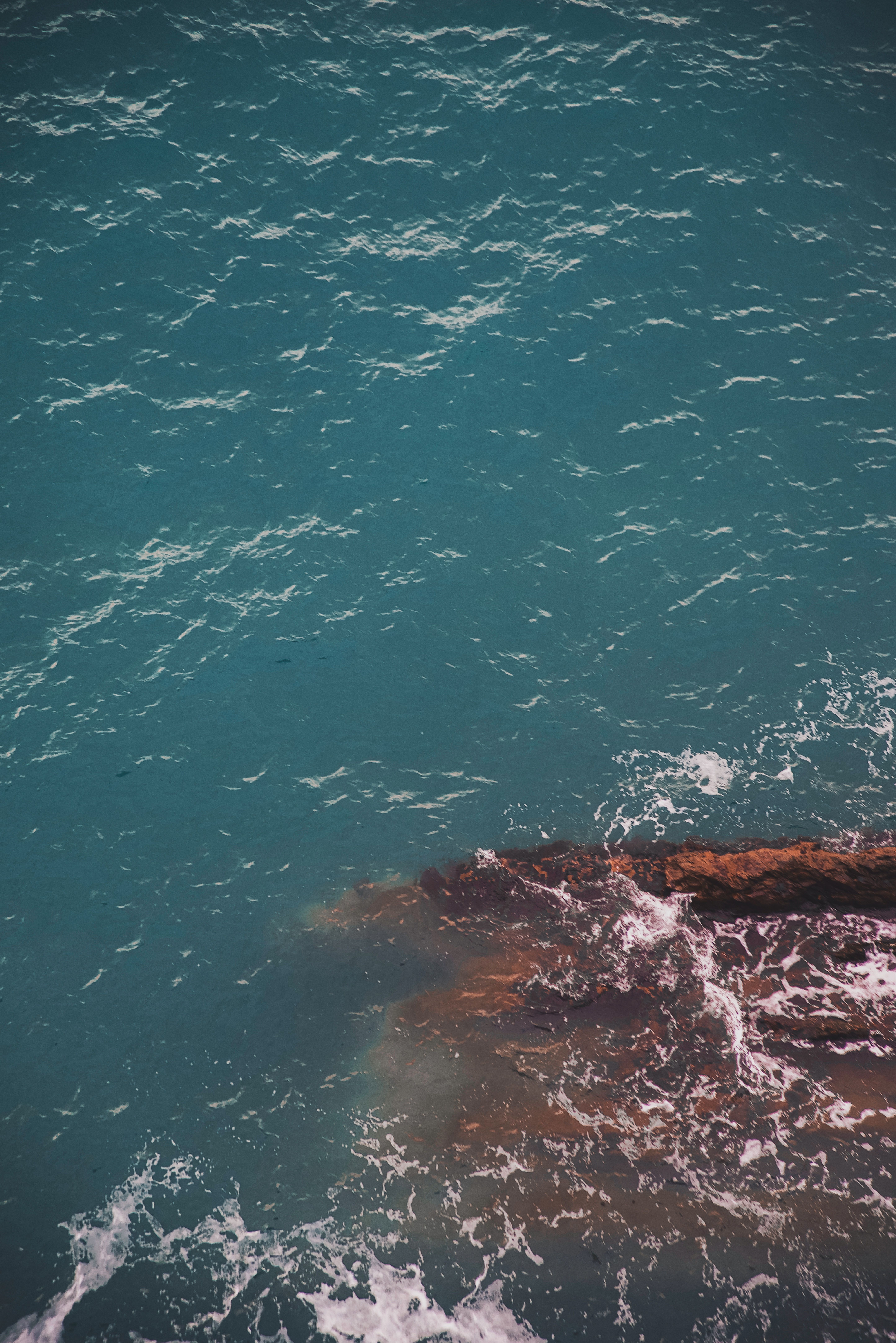 A high angle view of ocean waves crashing against a rock formation, displaying dynamic textures.