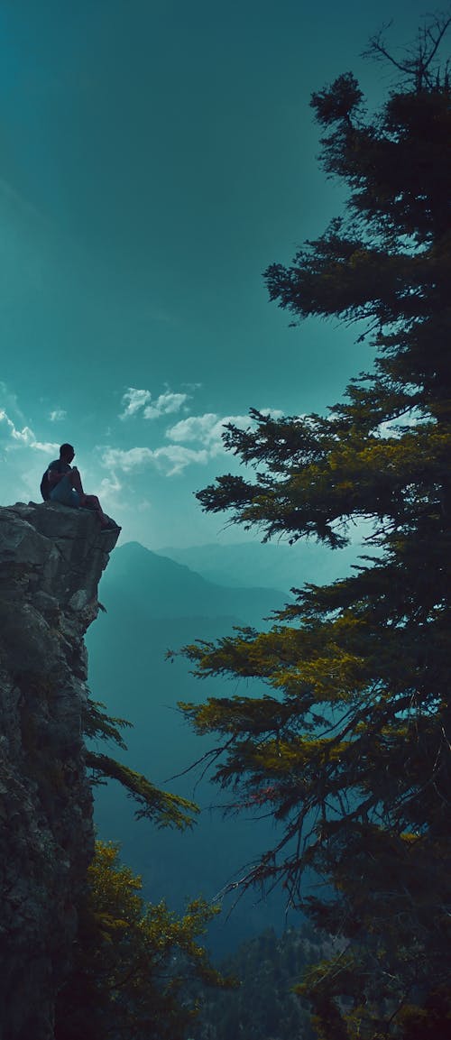 Silhouette of a Person Sitting on a Cliff
