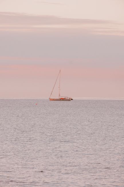 A sailboat glides on the calm ocean under a pastel sunset, capturing tranquility and adventure.