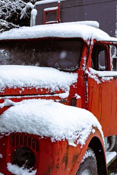 A vintage red truck parked outdoors, blanketed by fresh winter snowfall, creates a picturesque winter scene.