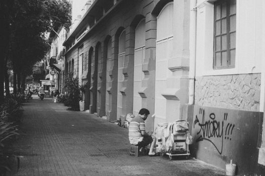 Black and white photo of a man painting graffiti on a city building.