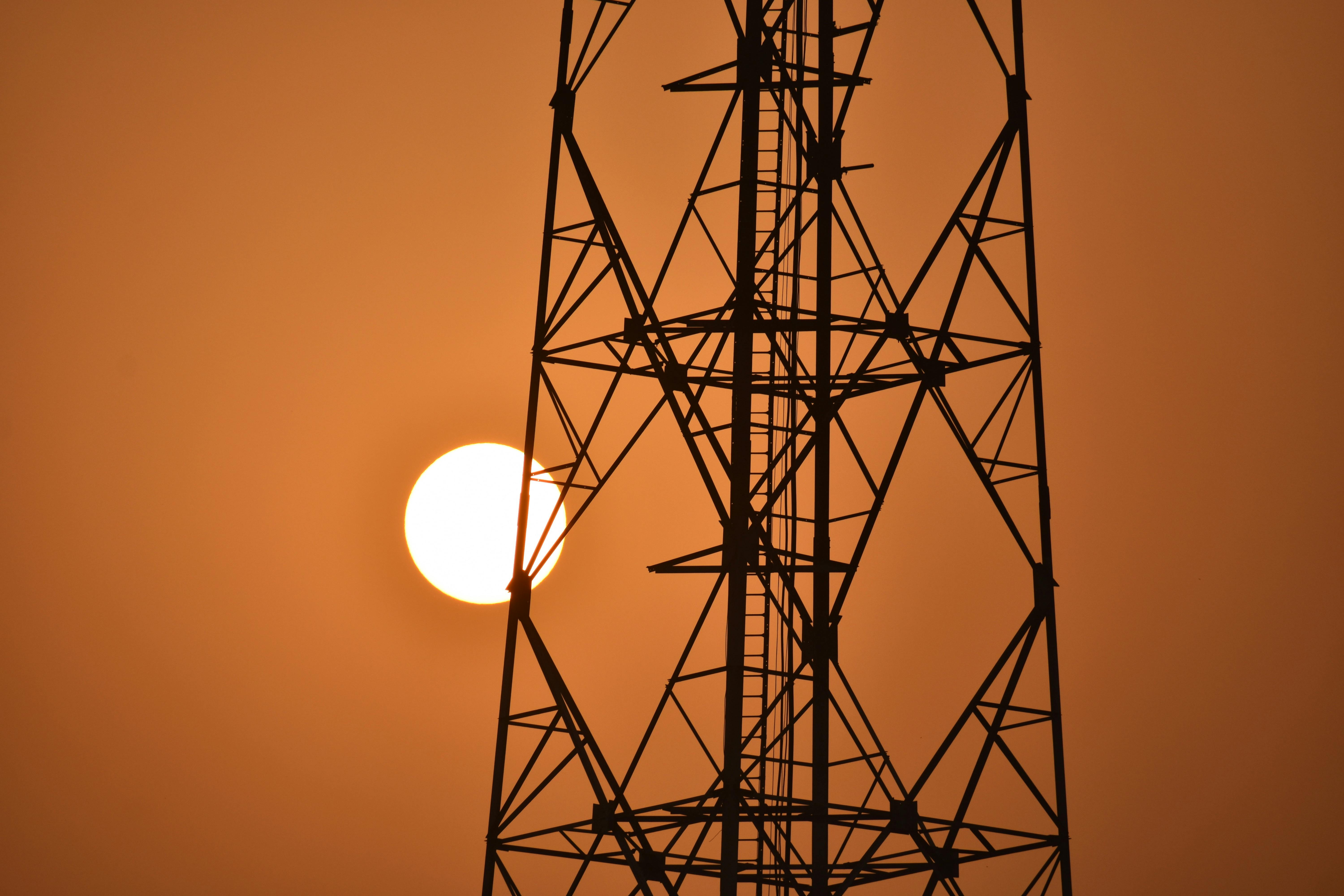 Dramatic silhouette of a power tower against a vibrant orange sunset, symbolizing energy.