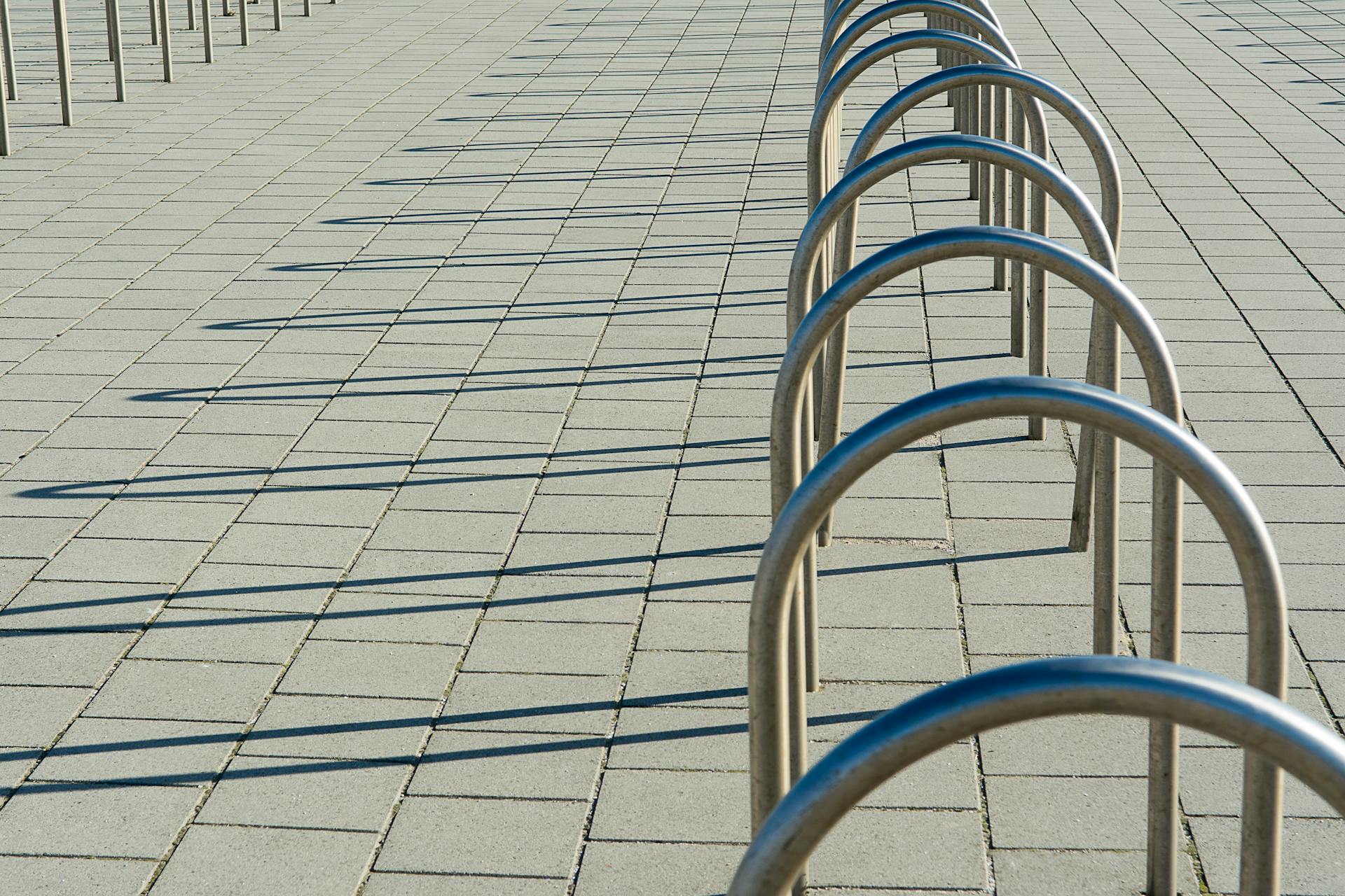 Curved metal bike racks creating geometric shadow patterns on sunny pavement.