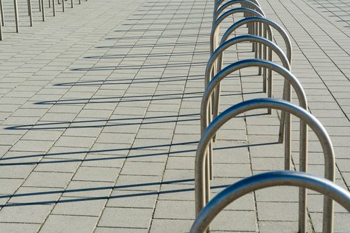 Free Curved metal bike racks creating geometric shadow patterns on sunny pavement. Stock Photo