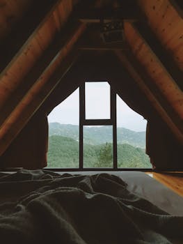 Charming A-frame attic with a window view of peaceful mountains framed by curtains, ideal for relaxation.