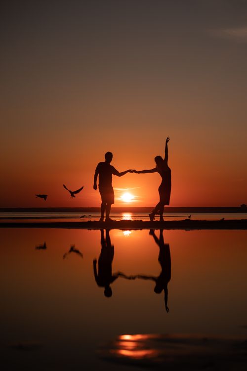 Free A couple holding hands and dancing at sunset on a scenic beach. Stock Photo