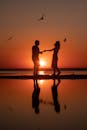日落时分，一对夫妇在海滩上跳舞的剪影，鸟儿在上面飞翔，水面倒影