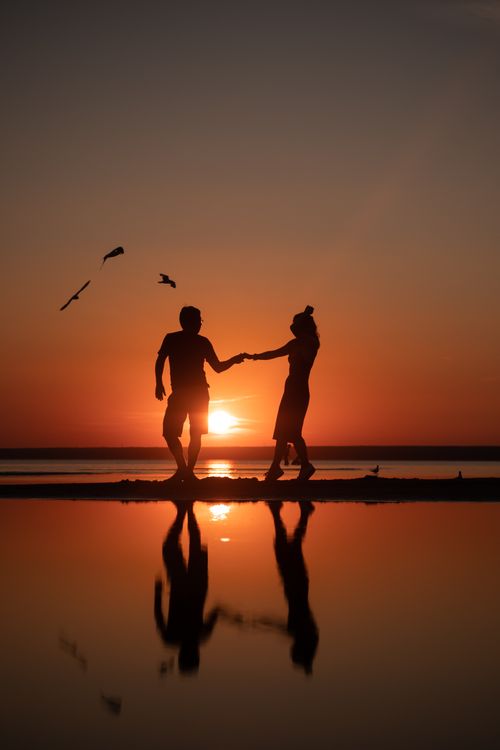 Free Silhouette of a couple holding hands on the beach at sunset, creating a romantic scene. Stock Photo