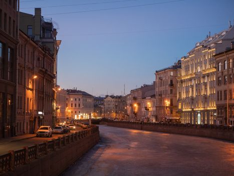 A serene winter cityscape of St. Petersburg with illuminated historic buildings along a frozen canal at dusk.