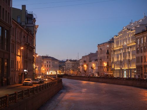 Free A serene winter cityscape of St. Petersburg with illuminated historic buildings along a frozen canal at dusk. Stock Photo
